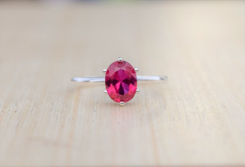 May include: A silver ring with a large, oval-shaped, bright red gemstone.