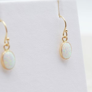 May include: A pair of gold earrings with oval-shaped white opal stones.