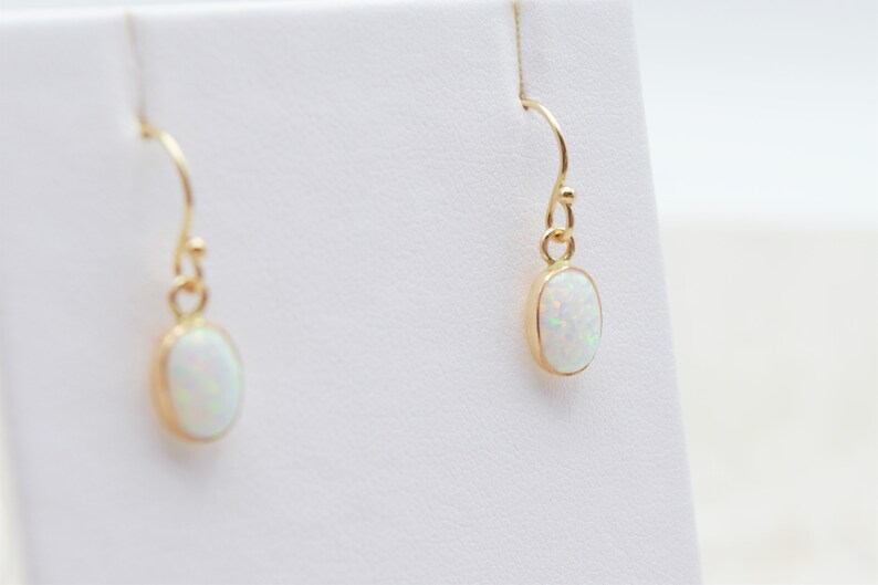 May include: A pair of gold earrings with oval-shaped white opal stones.