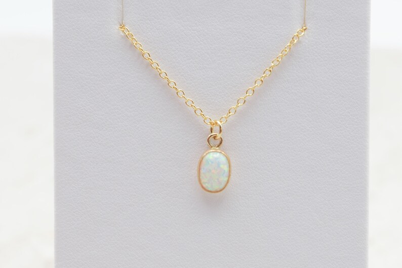 May include: A delicate gold chain necklace with a small oval opal pendant. The opal is a milky white color.