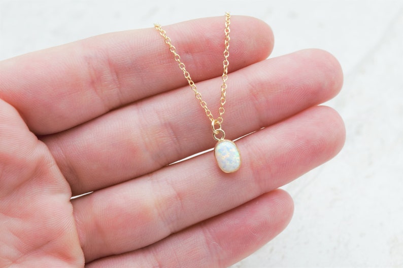 May include: A delicate gold chain necklace with a small oval opal pendant. The opal is white with a slight iridescent shimmer.