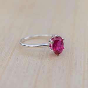 May include: A silver ring with a large, oval-shaped, bright pink gemstone.