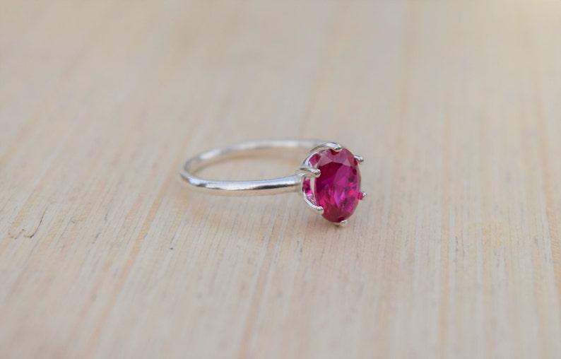 May include: A silver ring with a large, oval-shaped, bright pink gemstone.