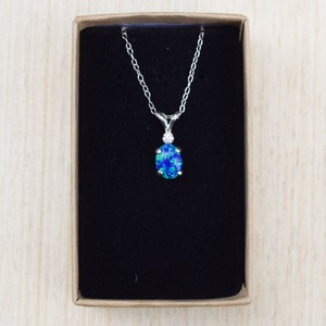 May include: A silver chain necklace with a blue opal pendant in a black velvet box.