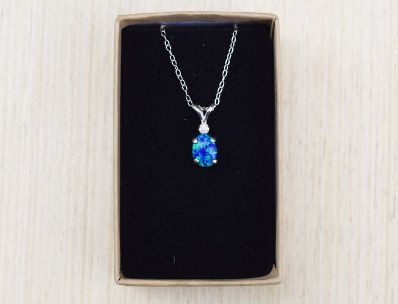 May include: A silver chain necklace with a blue opal pendant in a black velvet box.