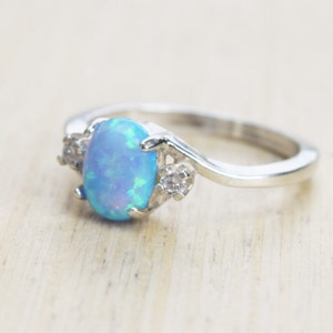 May include: A silver ring with a blue opal gemstone and two smaller clear gemstones.