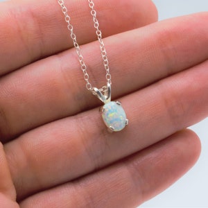 Puede incluir: Un collar de cadena de plata con un colgante de &oacute;palo blanco. El &oacute;palo tiene forma ovalada y tiene un delicado engaste de plata.