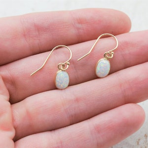 May include: A pair of gold earrings with white opal stones. The earrings are oval shaped and dangle from a simple hook.