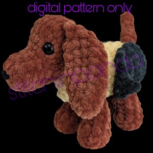 Peut inclure: Un chien en peluche marron avec de grandes oreilles tombantes, des yeux noirs et une petite queue. Le chien a un ventre crème et une tache bleu foncé sur le dos. Les mots "digital pattern only" sont écrits en violet au-dessus du chien.