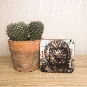 May include: Square coaster featuring a detailed painting of a brown dog with expressive eyes. The artwork has a textured appearance with visible brushstrokes. The coaster is placed on a wooden surface next to a potted cactus.