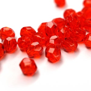 Könnte beinhalten: Ein Haufen leuchtend roter, facettierter Glasperlen, verstreut auf weißem Hintergrund.