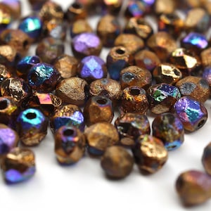 May include: A pile of iridescent bronze glass beads with a faceted, irregular shape. The beads have a metallic sheen and a textured surface.