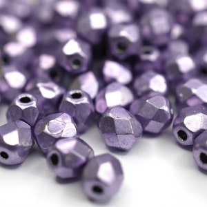 May include: A close-up of a pile of small, faceted, metallic purple beads. The beads have a shiny, iridescent finish.
