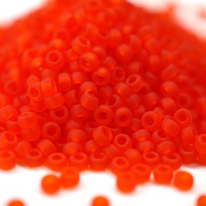 Könnte beinhalten: Ein Haufen kleiner, leuchtend orangefarbener Glasperlen. Die Perlen sind rund und haben eine glatte, matte Oberfläche.