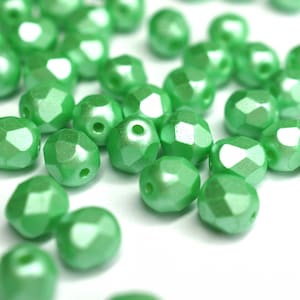 May include: A close-up of a group of green faceted glass beads. The beads are iridescent and have a slightly pearlescent finish.