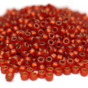 Könnte beinhalten: Ein Haufen kleiner, runder, roter Glasperlen mit schimmerndem Finish. Die Perlen haben ein kleines Loch in der Mitte zum Auf fädeln.