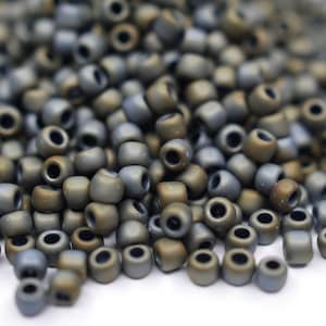Könnte beinhalten: Ein Haufen kleiner, runder, metallischer Perlen in Grautönen und Braun. Die Perlen haben eine matte Oberfläche und sind auf einer weißen Oberfläche verstreut.