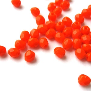 Könnte beinhalten: Eine Streuung von leuchtend orangefarbenen facettierten Glasperlen auf einer weißen Oberfläche.