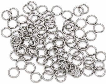 May include: A collection of numerous small, circular metal jump rings with a polished silver-tone finish. Each individual ring features a single cut opening, allowing them to be easily opened and closed for various jewelry making and craft projects.