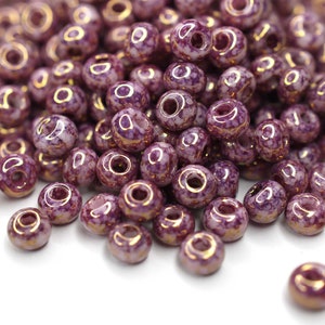 May include: A pile of purple and gold ceramic beads. The beads are round and have a speckled finish.