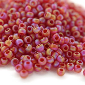 May include: A pile of small, round, iridescent beads in a reddish-pink color with a slight orange hue.