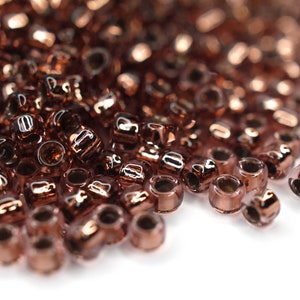 May include: A pile of small, round, copper-colored glass beads. The beads have a shiny, metallic finish.