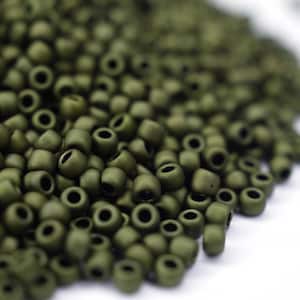 Puede incluir: Primer plano de un montón de pequeñas cuentas redondas de color verde oliva. Las cuentas son de vidrio y tienen un acabado mate.