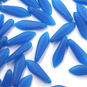 May include: A group of blue glass beads in a teardrop shape. The beads are frosted and have a matte finish.