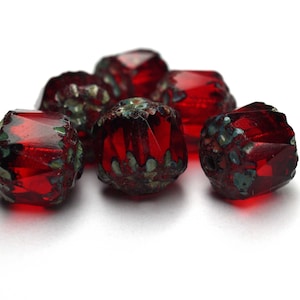 Könnte beinhalten: Sechs rote Glasperlen mit komplizierten Mustern. Die Perlen sind facettiert und haben eine glänzende Oberfläche.