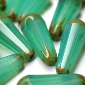 May include: A close-up of several green glass beads with brown flecks. The beads are teardrop shaped and have a glossy finish.