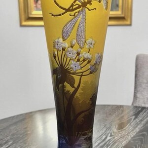 May include: A tall, yellow glass vase with a flared top and a dark base. The vase features a painted design of dragonflies, flowers, and a water scene. The vase is approximately 12 inches tall.