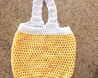 May include: A yellow and white crocheted tote bag with a single handle. The bag is made of a mesh material and has a rounded bottom.