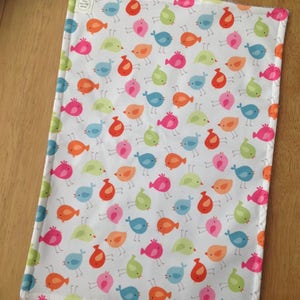 May include: A white fabric dish towel with a repeating pattern of colorful birds. The birds are in various shades of blue, green, orange, pink, and red.