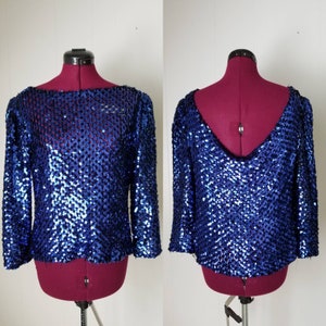 May include: A blue sequined top with long sleeves and a V-neckline. The top is on a dress form.