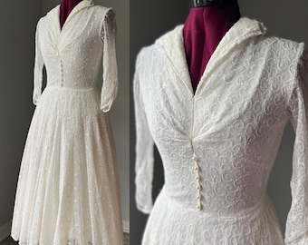 May include: A white lace dress with a V-neckline and 3/4 sleeves. The dress has a fitted bodice and a full skirt. The dress is decorated with pearl buttons down the front.