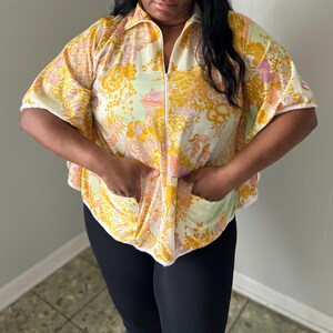 May include: A white, yellow, and orange patterned short-sleeved shirt with a zipper closure. The shirt has a collar and two pockets.