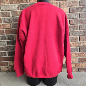 K&ouml;nnte beinhalten: Ein einfarbig rotes Langarm-Sweatshirt mit Rundhalsausschnitt und gerippten B&uuml;ndchen. Das Kleidungsst&uuml;ck wird auf einer Schaufensterpuppe pr&auml;sentiert und zeigt eine schlichte, musterlose R&uuml;ckansicht des Stoffes in einem durchgehend kr&auml;ftigen Rot.