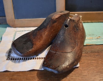 May include: Two antique wooden shoe lasts, one brown and one dark brown, with a hole in the top of each. The lasts are sitting on a white doily.