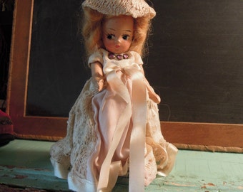 May include: A vintage porcelain doll wearing a white lace and pink satin dress with a pink satin bow and a white crocheted hat.