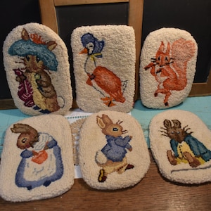 May include: Six handmade needlepoint wall hangings featuring various characters from the children's book, Peter Rabbit. The characters include Peter Rabbit, Benjamin Bunny, Squirrel Nutkin, Jemima Puddle-Duck, Mrs. Tiggy-Winkle, and Tom Kitten.