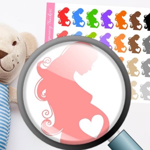 May include: A sheet of colorful pregnancy tracker stickers featuring a silhouette of a pregnant person with a heart. The stickers are in various colors, including red, blue, green, and orange. A plush teddy bear is in the background.