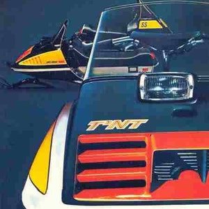 May include: A white, black and red snowmobile with a yellow stripe. The snowmobile has a black seat and a black windscreen. The snowmobile has a black headlight and a black grille. The snowmobile has the word "TNT" written on the front. The snowmobile has the word "SS" written on the top of the windscreen.