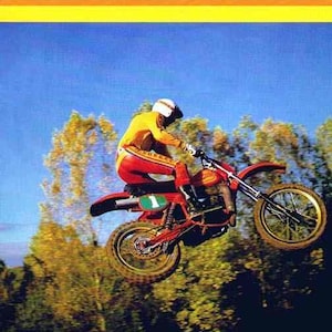 May include: A red and white motocross motorcycle with a rider in a yellow and red racing suit, jumping over a dirt track. The motorcycle has a green number "1" on the side. The text "MAICO the ultimate racing machine 250 400 490" is at the top of the image.
