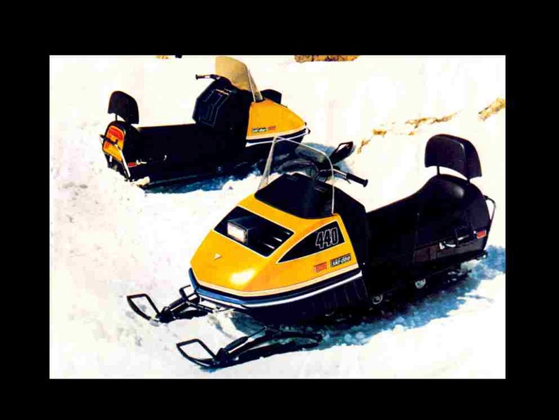 May include: Two yellow and black snowmobiles parked in the snow. The snowmobile in the foreground has a black seat and a 440cc engine. The snowmobile in the background has a yellow seat.