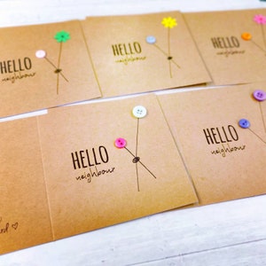 May include: A set of six handmade greeting cards with the text "Hello neighbour" on each card. Each card features a different coloured button and a simple drawing of a flower stem.