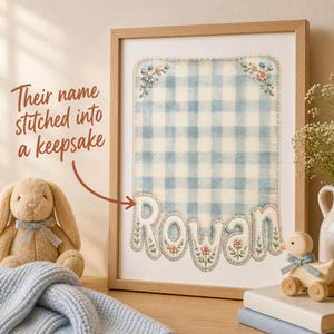 Peut inclure: Une impression encadrée présentant un fond en tissu vichy bleu clair et blanc avec des coins brodés de fleurs et le nom Rowan cousu en grandes lettres rembourrées décorées de petits motifs floraux roses et verts en bas.