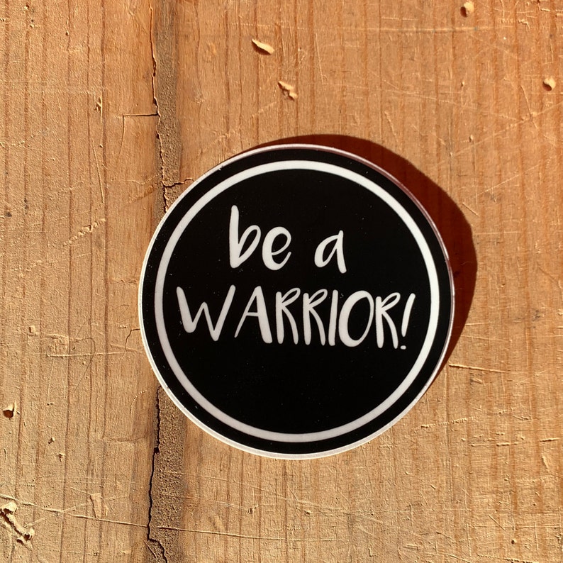 May include: Black and white sticker with the text "be a warrior!" on a wood background.