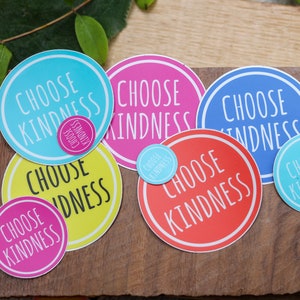 May include: A collection of seven round stickers with the phrase "Choose Kindness" written in white on a variety of colored backgrounds, including blue, pink, yellow, and red.