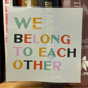 May include: A square sticker with the words "WE BELONG TO EACH OTHER" in various colors. The words are stacked vertically, with each word in a different color, including teal, yellow, black, red, orange, pink, and green.