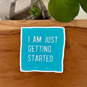 May include: A turquoise blue sticker with white text that reads "I am just getting started".
